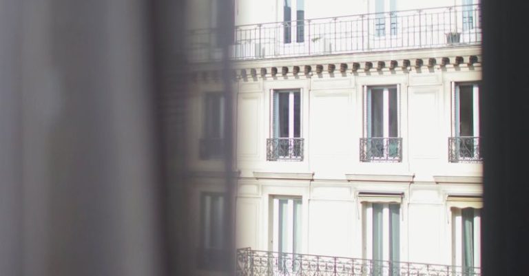 El Born Stay - Hotel with elegant balconies and bay windows in Paris as seen from opposite building through slightly ajar window curtains on sunny day