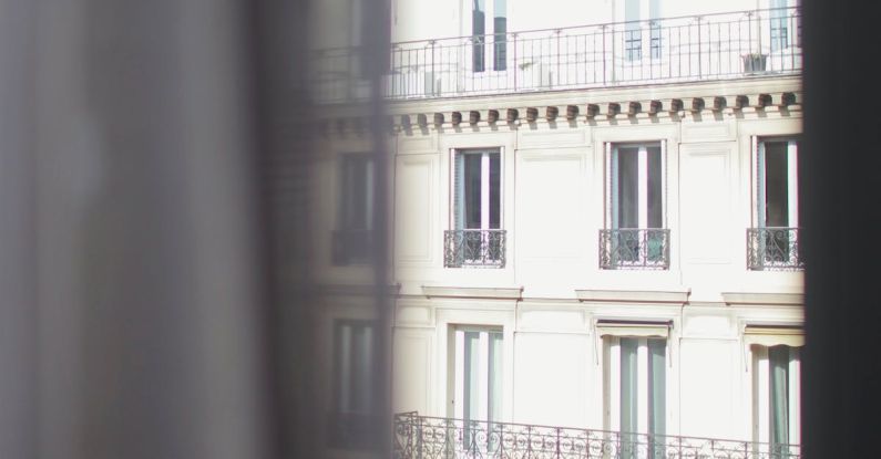 El Born Stay - Hotel with elegant balconies and bay windows in Paris as seen from opposite building through slightly ajar window curtains on sunny day