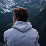 Solo Travel Barcelona - A Man in White Hoodie Sitting on a Rock Across the Mountains