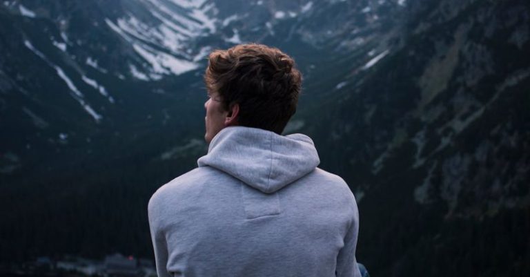 Solo Travel Barcelona - A Man in White Hoodie Sitting on a Rock Across the Mountains