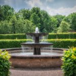 Fountain - a water fountain surrounded by hedges and trees
